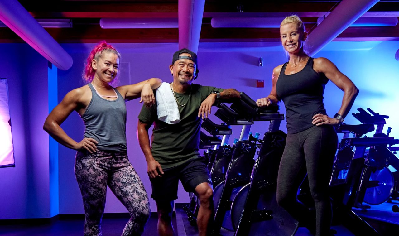 Three members smiling beside the bikes in the spin studio